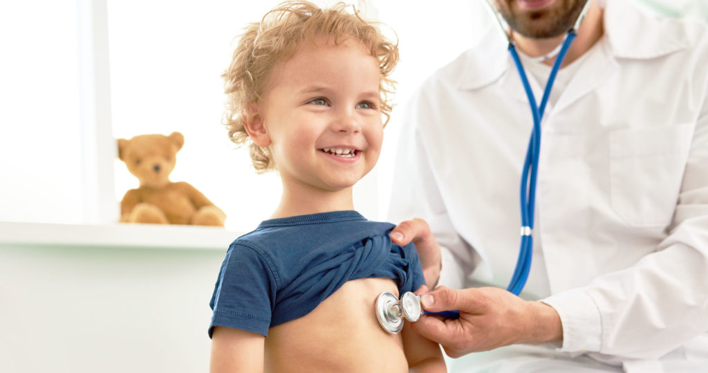 Clinician checking heartbeat of child in blue shirt with stethoscope.